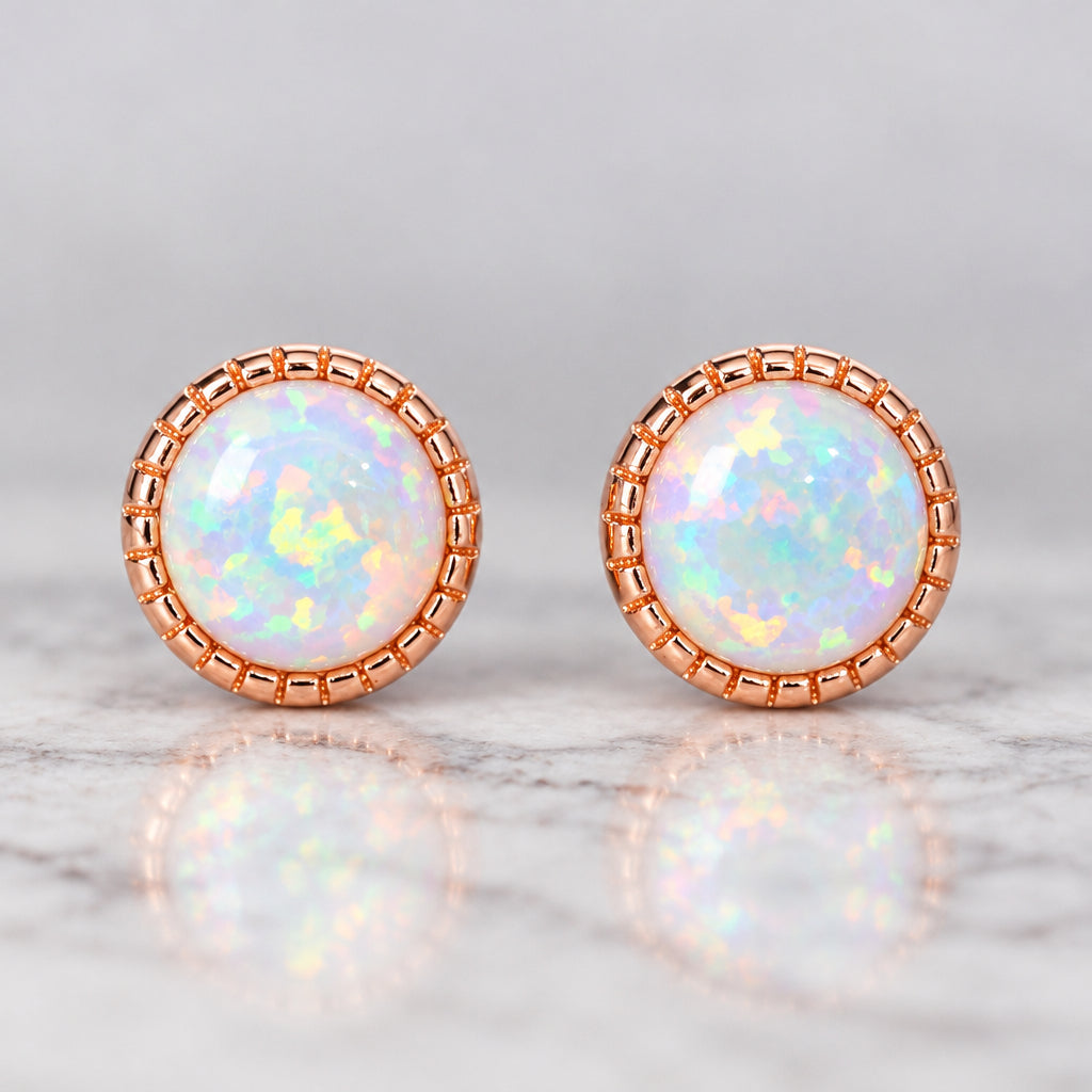 Pair of round rose gold white opal stud earrings on a marble surface
