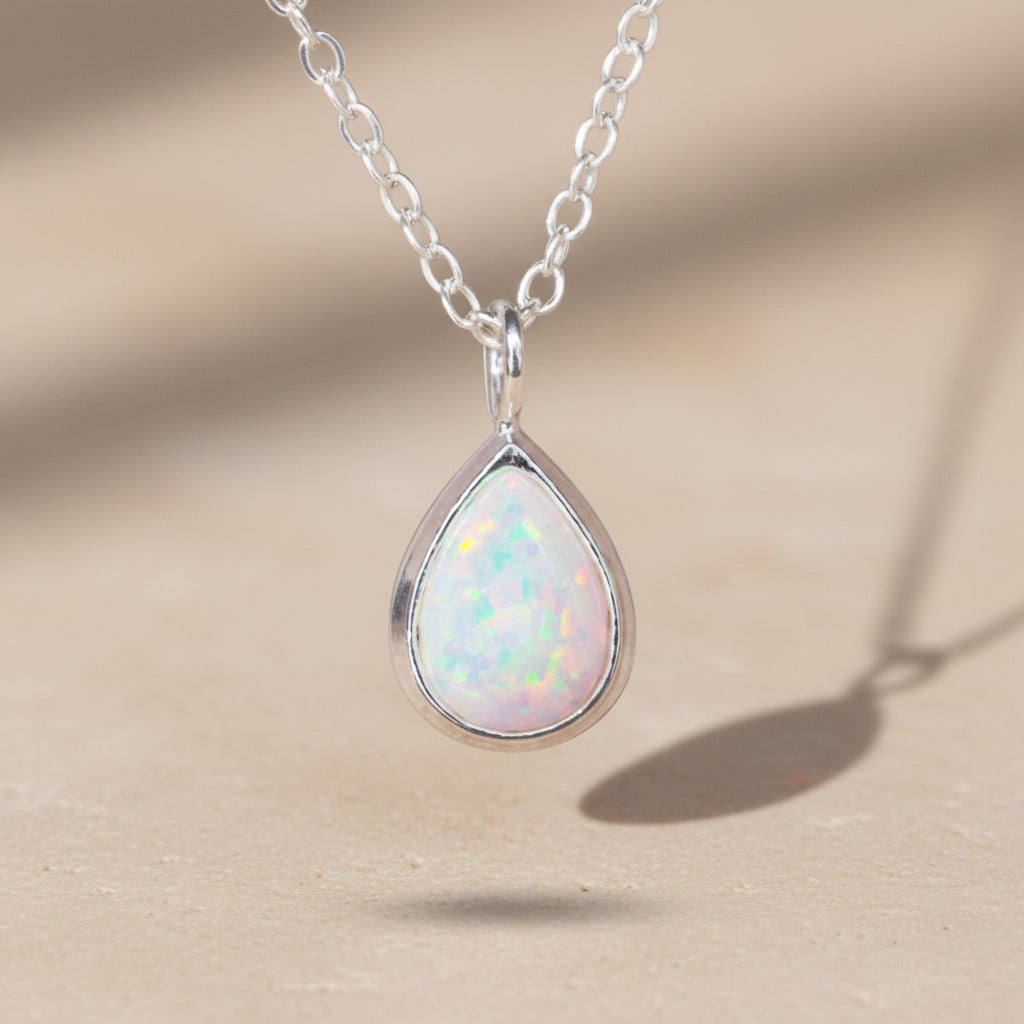 Teardrop-shaped opal pendant on a silver chain against a light background