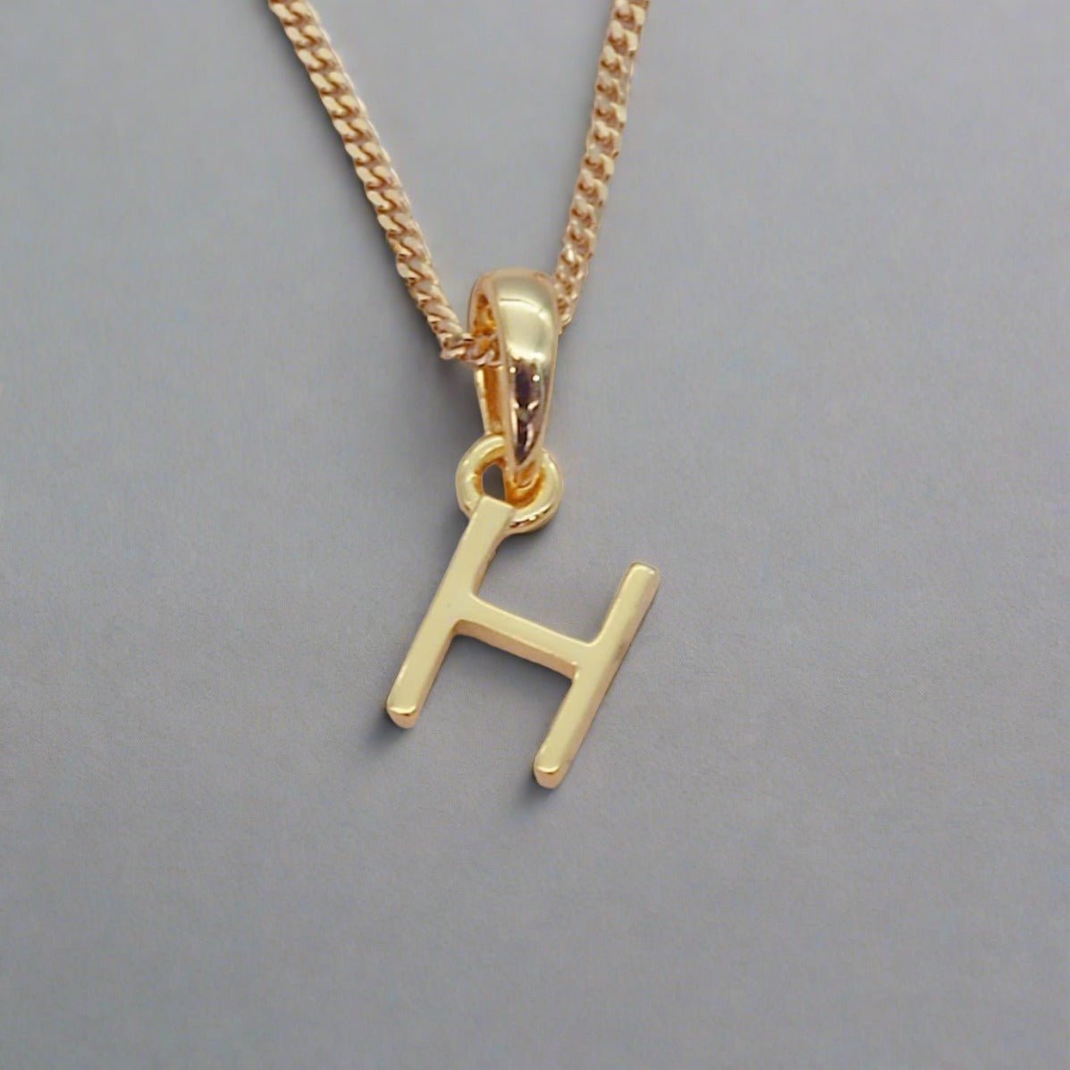 gold initial h necklace on a grey background