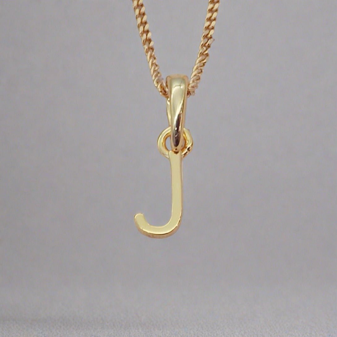 Gold necklace with a 'J' pendant on a gray background