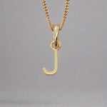 Gold necklace with a 'J' pendant on a gray background