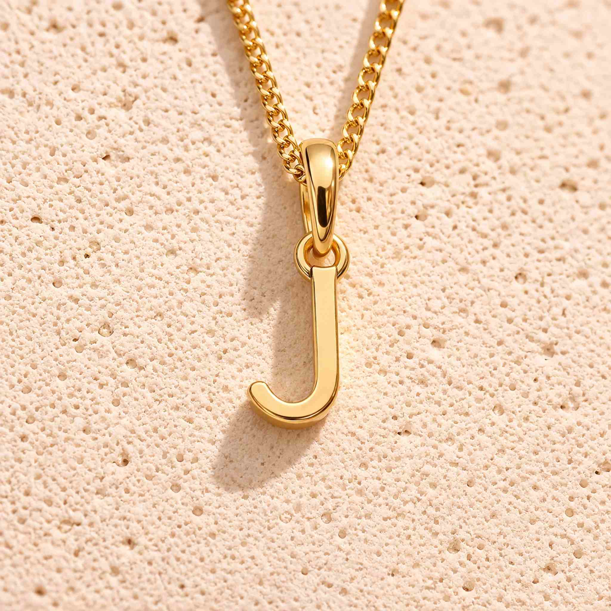 Gold Initial necklace with a 'J' pendant on a grey background. a letter charm option to personalise Necklaces