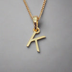 Gold necklace with a 'K' initial pendant on a gray background