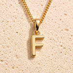 close up of a gold initial f pendant necklace on a light stone background - a letter charm option to personalise either a Zodiac or Birthstone Necklace