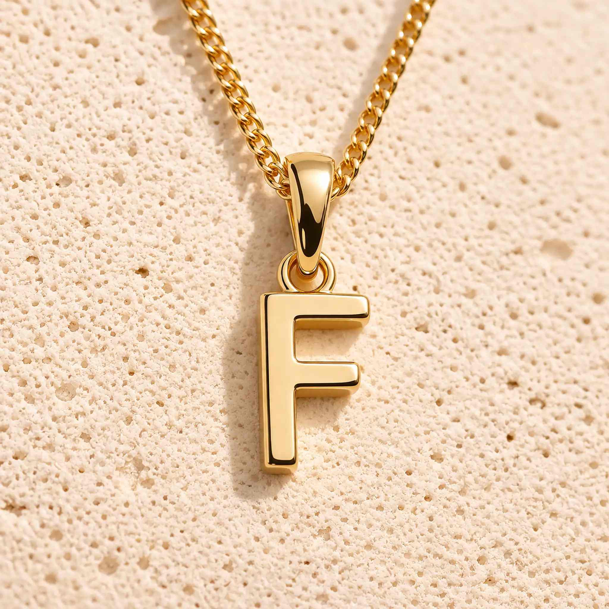 close up of a gold initial f pendant necklace on a light stone background - a letter charm option to personalise either a Zodiac or Birthstone Necklace