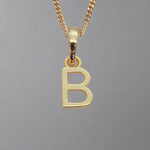 gold initial 'B' pendant necklace on a grey background