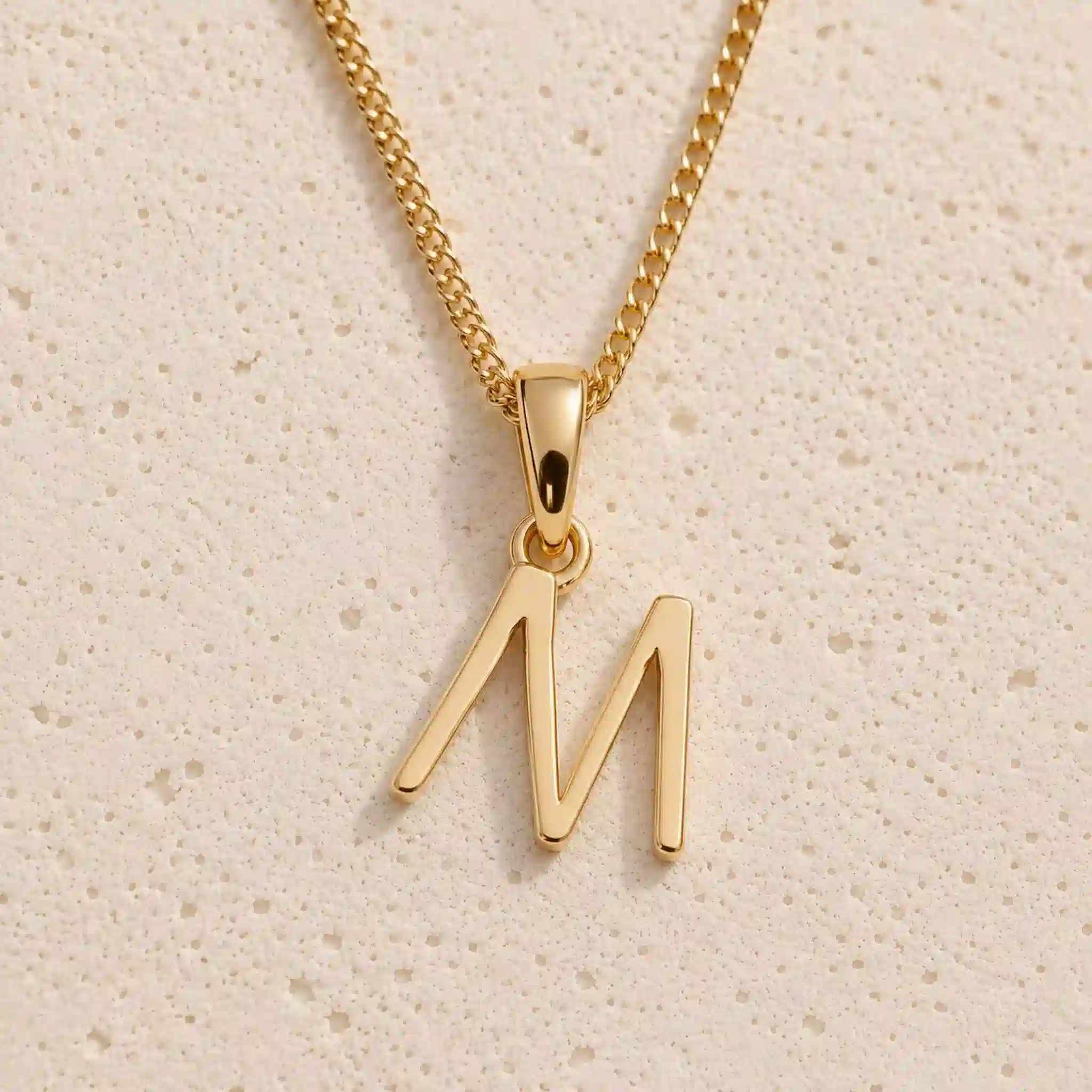Close-up of gold initial necklace with a M letter charm on a fine gold chain; a letter charm option to personalise Necklaces