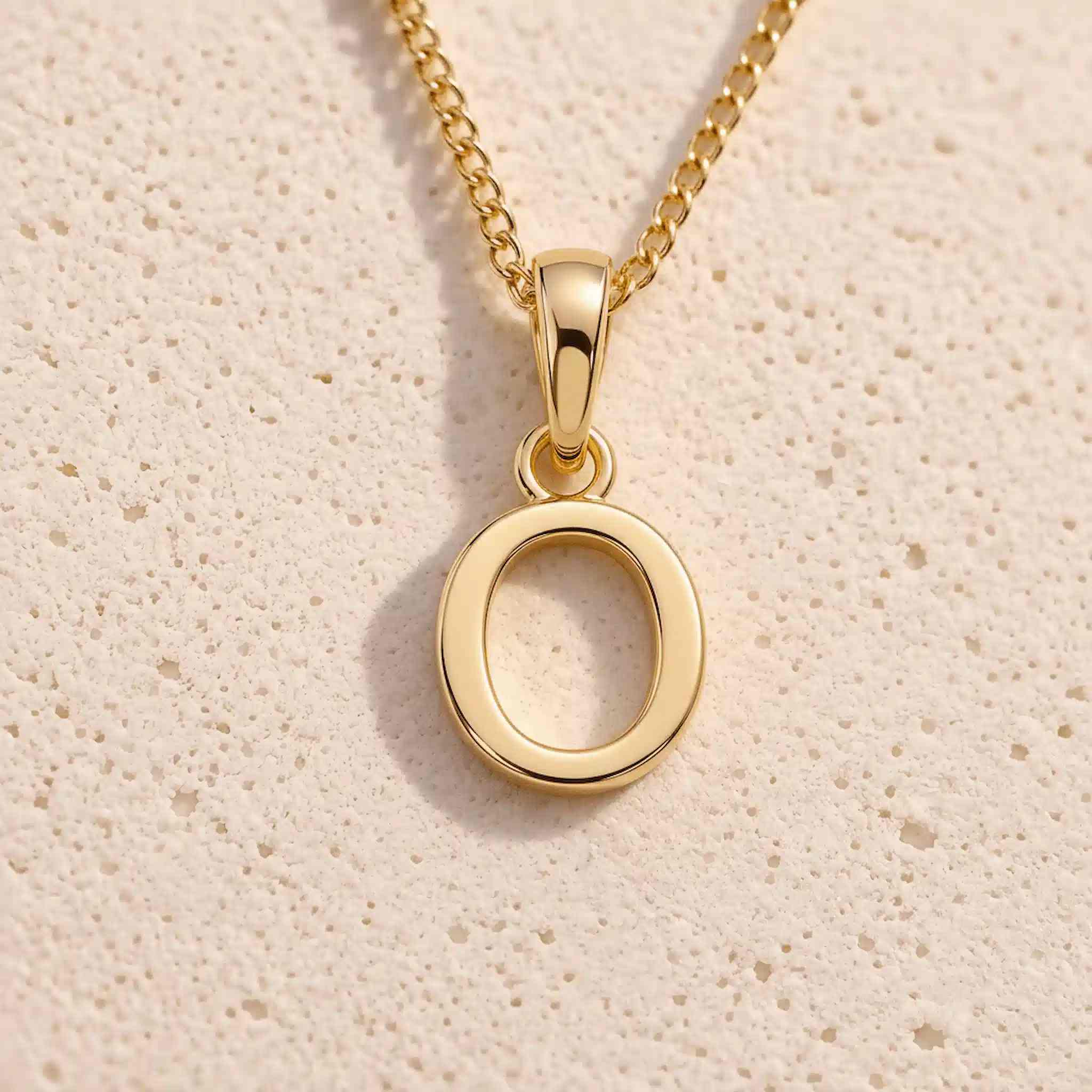 Close-up of gold initial necklace with a O letter charm on a fine gold chain; a letter charm option to personalise Necklaces