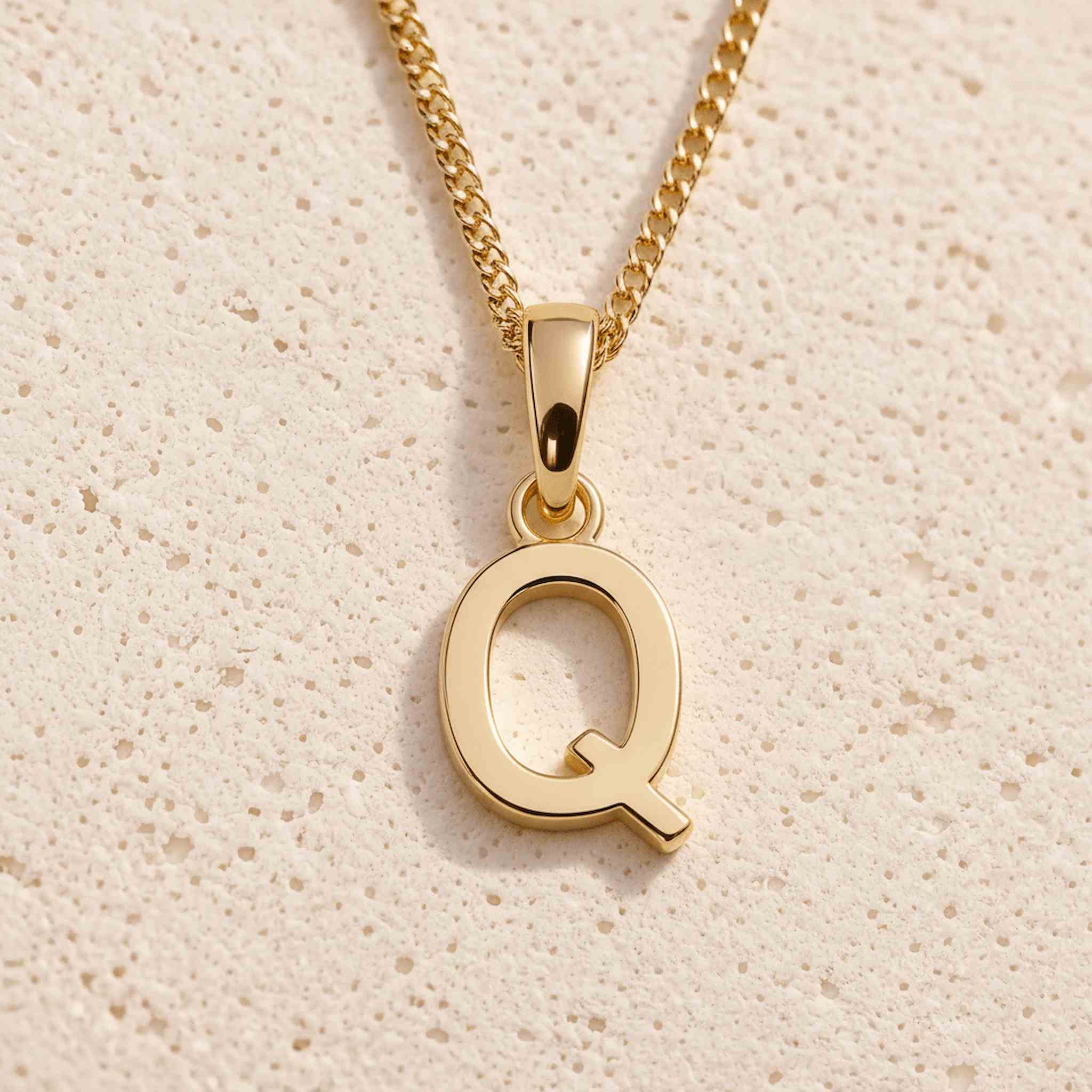 Close-up of gold initial necklace with a Q letter charm on a fine gold chain; a letter charm option to personalise Necklaces