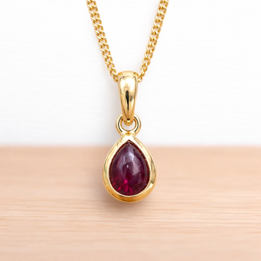 Gold pendant with a red ruby gemstone on a wooden surface