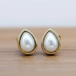 Pearl earrings with gold teardrop-shaped settings on a wooden surface.