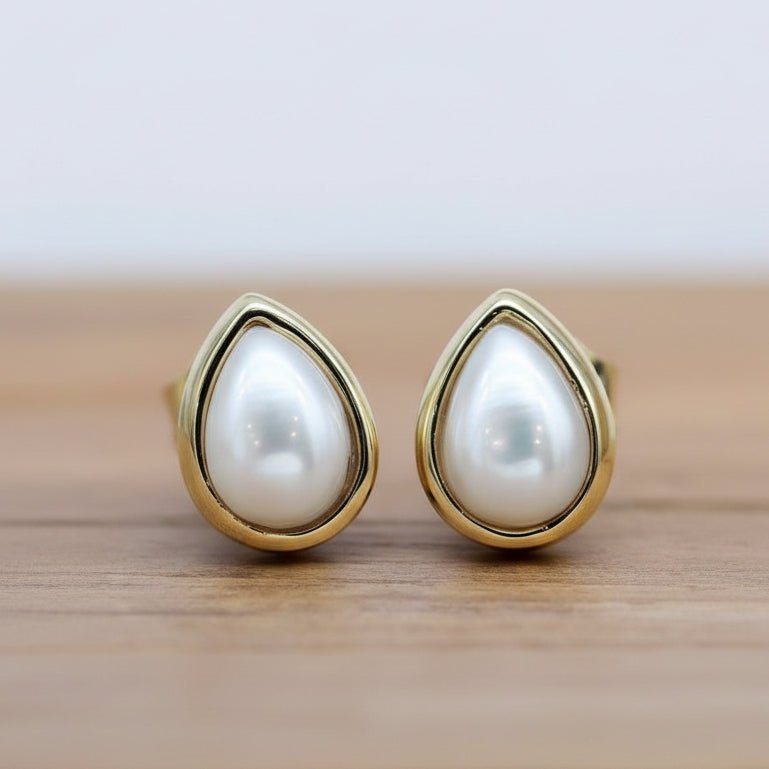 Pearl earrings with gold teardrop-shaped settings on a wooden surface.