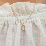 Gold necklace with a teardrop-shaped natural mother of pearl pendant being worn by a person with a white blouse