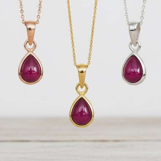 Three pendants with teardrop-shaped red ruby gemstones on gold, rose gold, and silver chains.