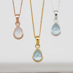 Three teardrop-shaped aquamarine pendants on silver, gold and rose gold chains against a white background.