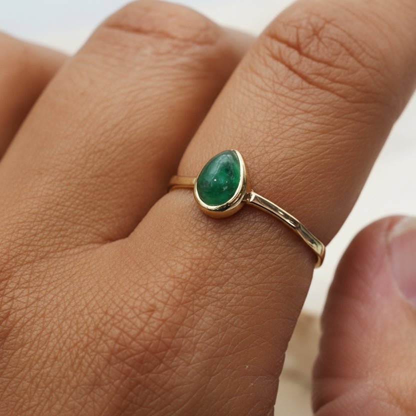 Gold ring with a teard drop shaped natural emerald gemstone on a person's finger
