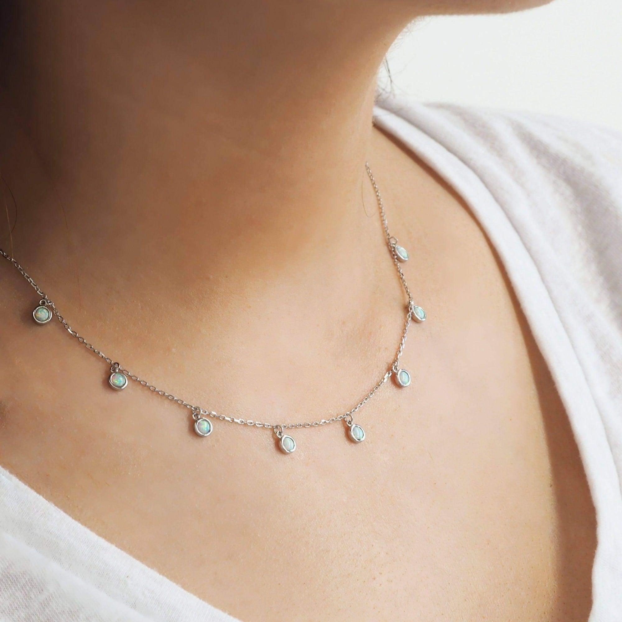 Delicate Sterling Silver necklace with small round opal pendants on a person wearing a white top.