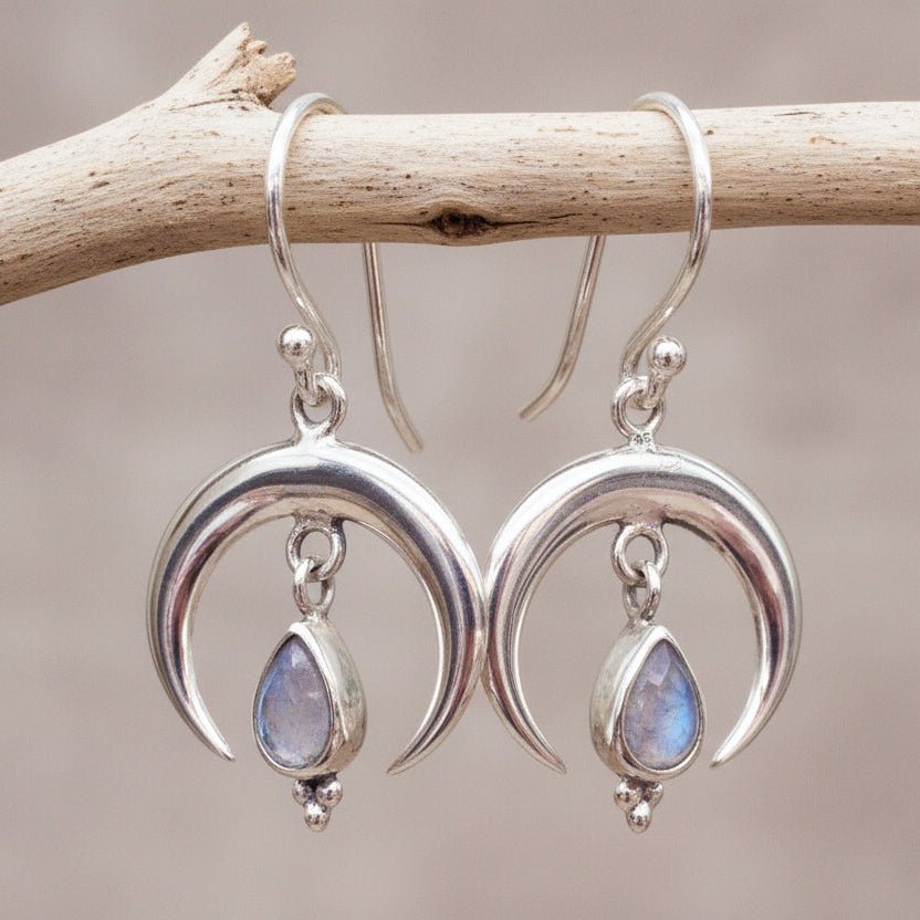Sterling Silver moon-shaped earrings with teardrop Moonstones hanging on a branch.