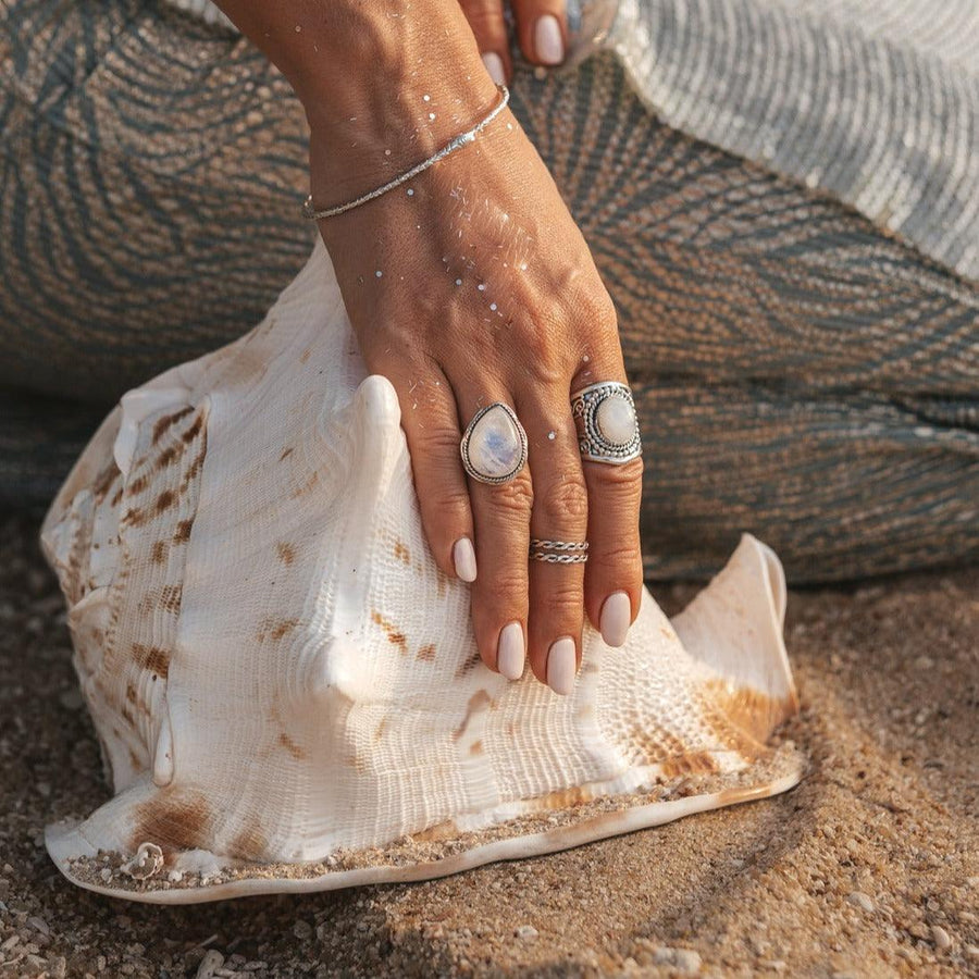 woman holding large shell on the beach and wearing sterling silver moonstone rings - womens moonstone jewellery by australian jewellery brand indie and harper