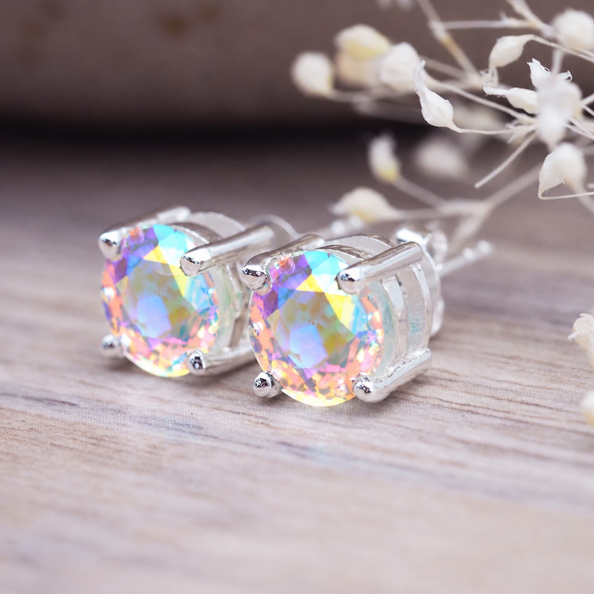 Pair of faceted mystic quartz studs on a light wooden surface
