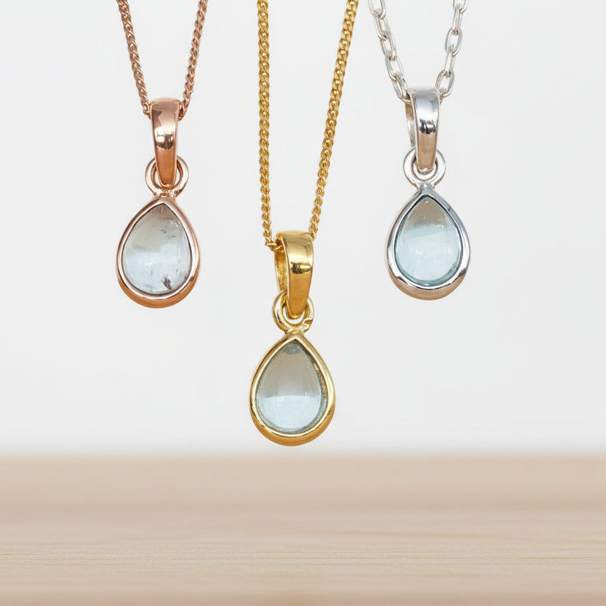 Three teardrop-shaped topaz pendants on rose gold, gold and silver chains against a white background