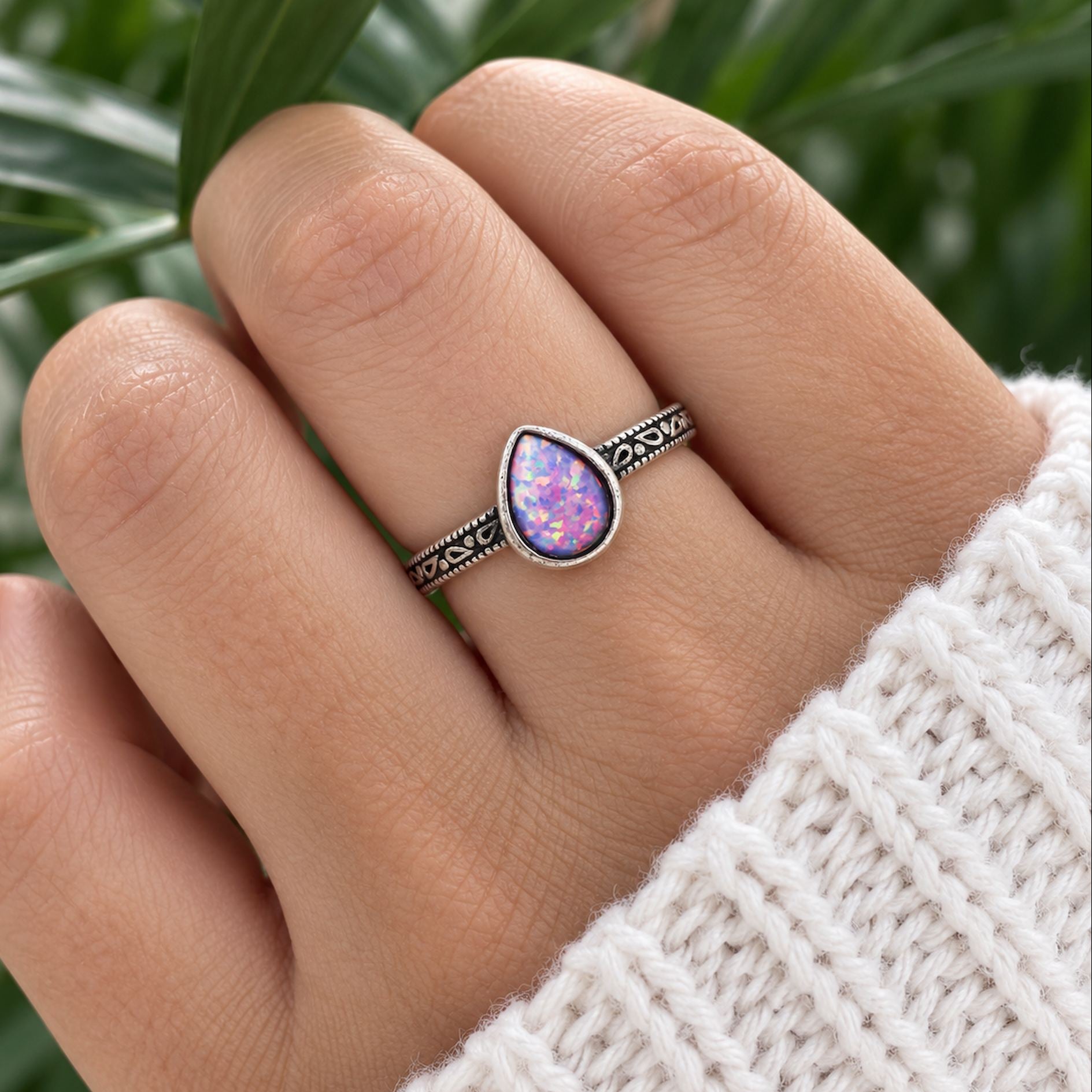 Hand wearing a sterling silver teardrop purple opal ring against blurred greenery
