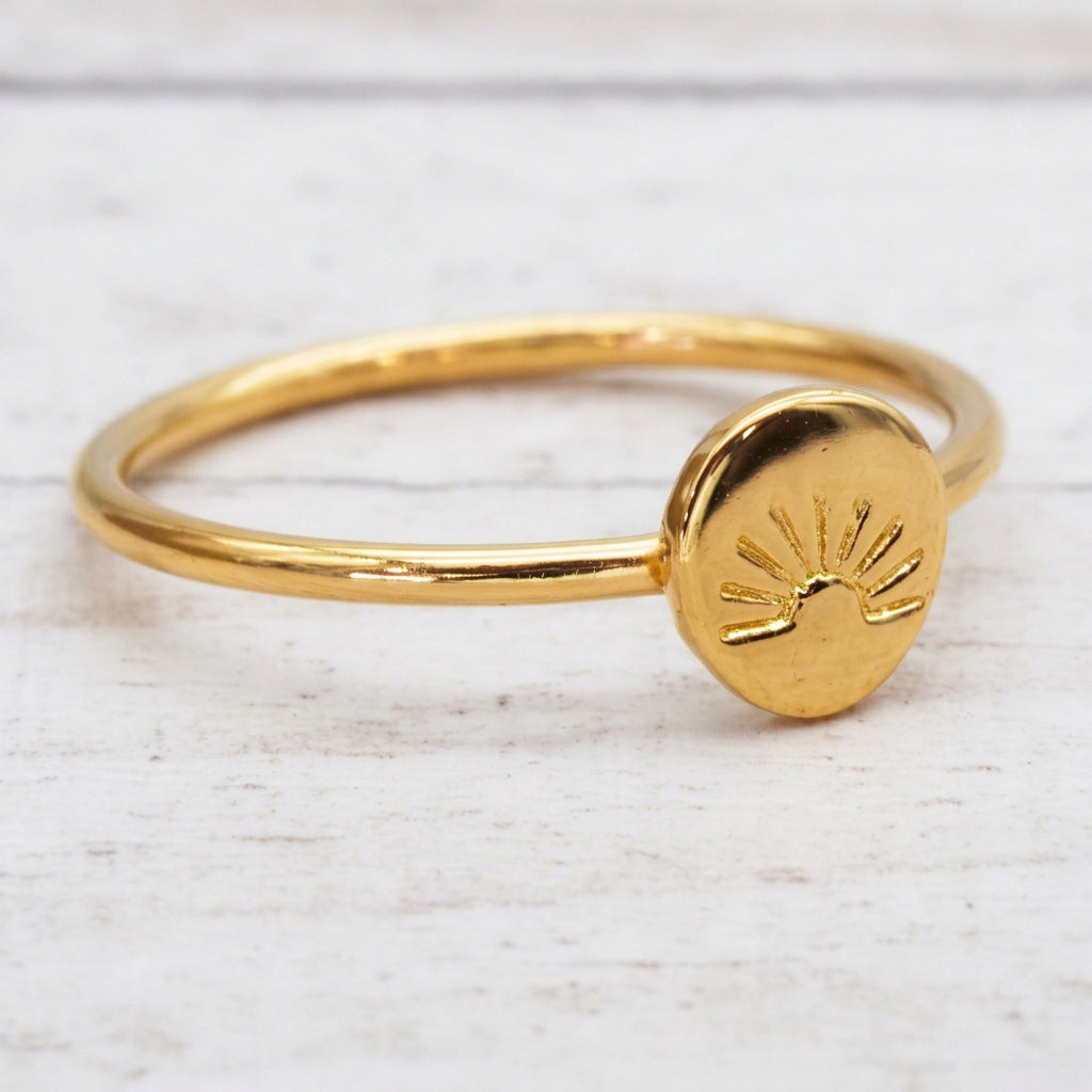 Gold rising sun ring with an engraved disc on a light wooden surface
