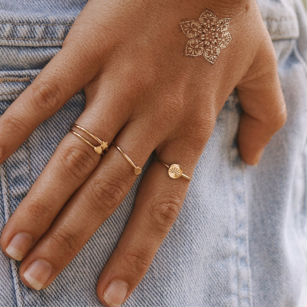 Hand on denim wearing dainty gold rings including the sun ring