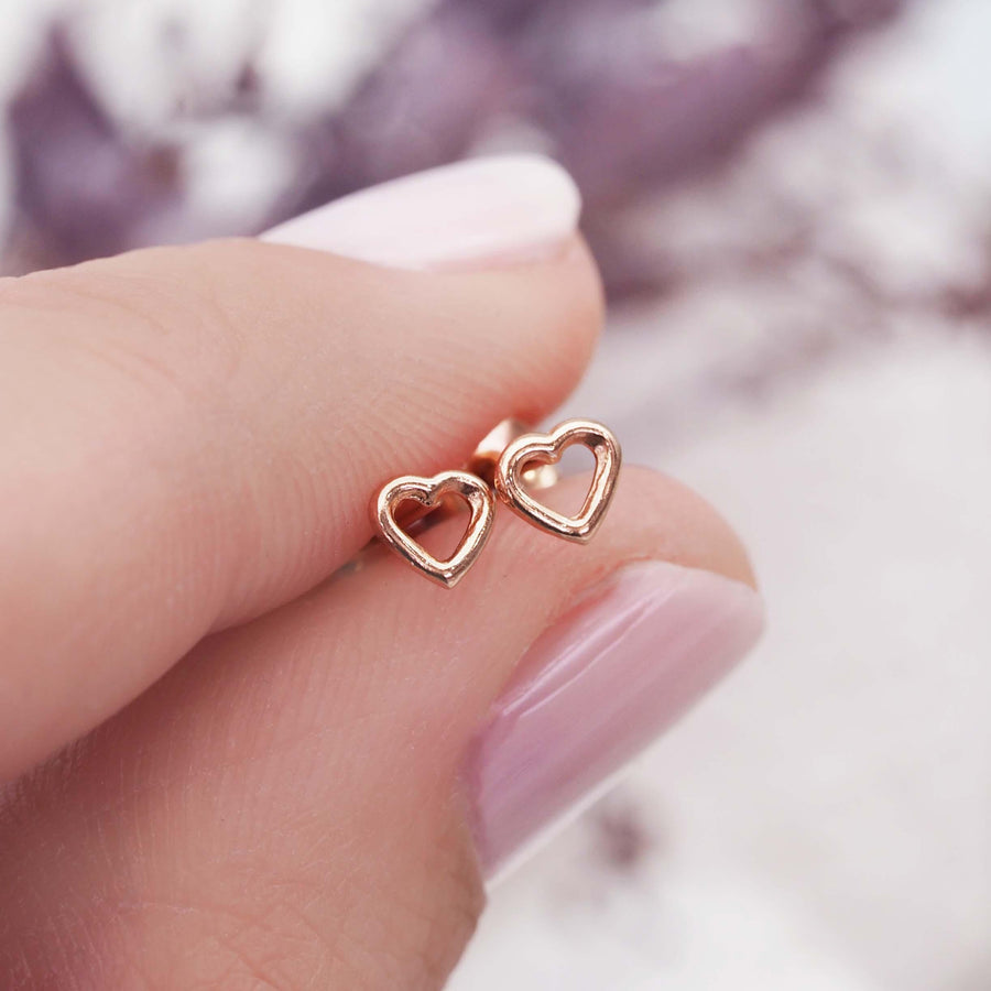Fingers holding Dainty heart shaped Rose Gold Earrings - womens rose gold jewellery 