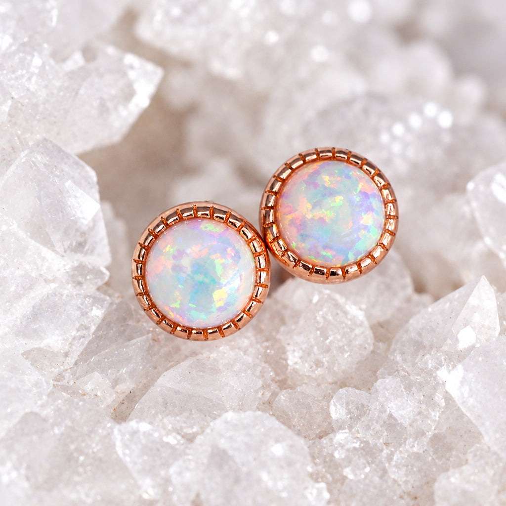 Round white opal earrings in rose gold settings on a white textured background