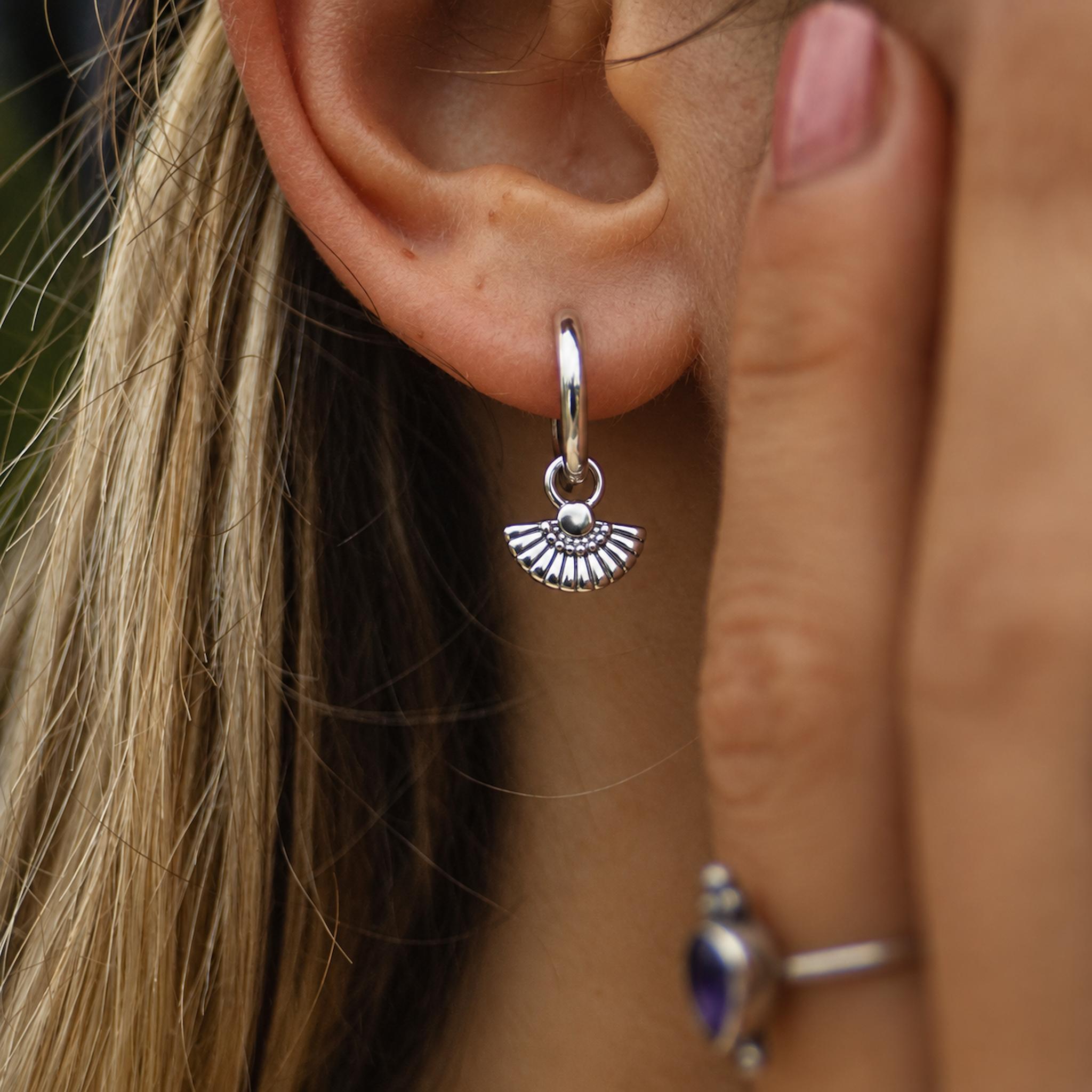 Close-up of a silver hoop earring with a small pendant worn by a person.