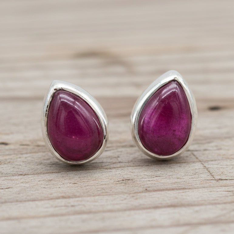 Teardrop-shaped ruby earrings with silver settings on a wooden surface