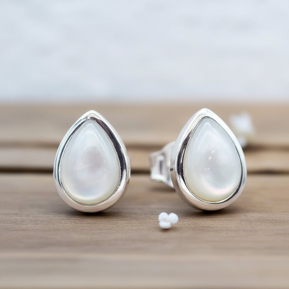Teardrop-shaped silver earrings with white pearls on a wooden surface.