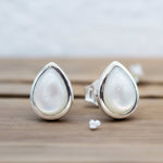 Teardrop-shaped silver earrings with white pearls on a wooden surface.