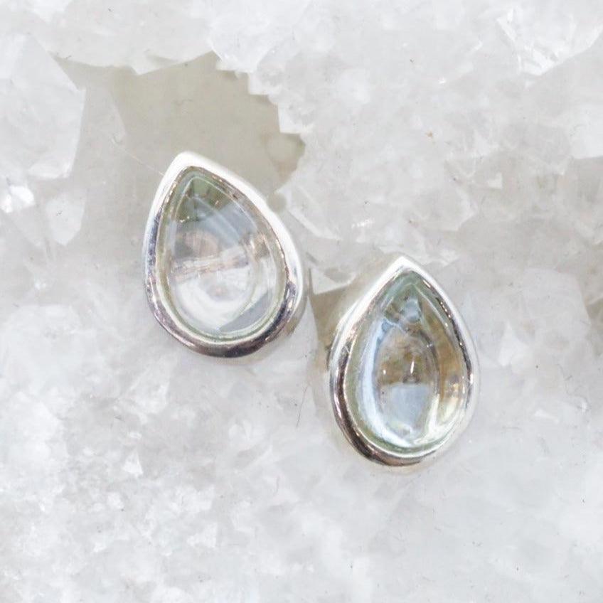 Teardrop-shaped silver earrings on a textured white surface with topaz gemstones