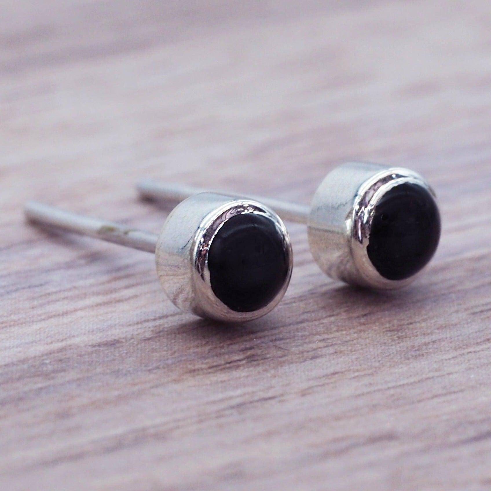 Dainty black Onyx gemstone stud earrings on a wooden surface