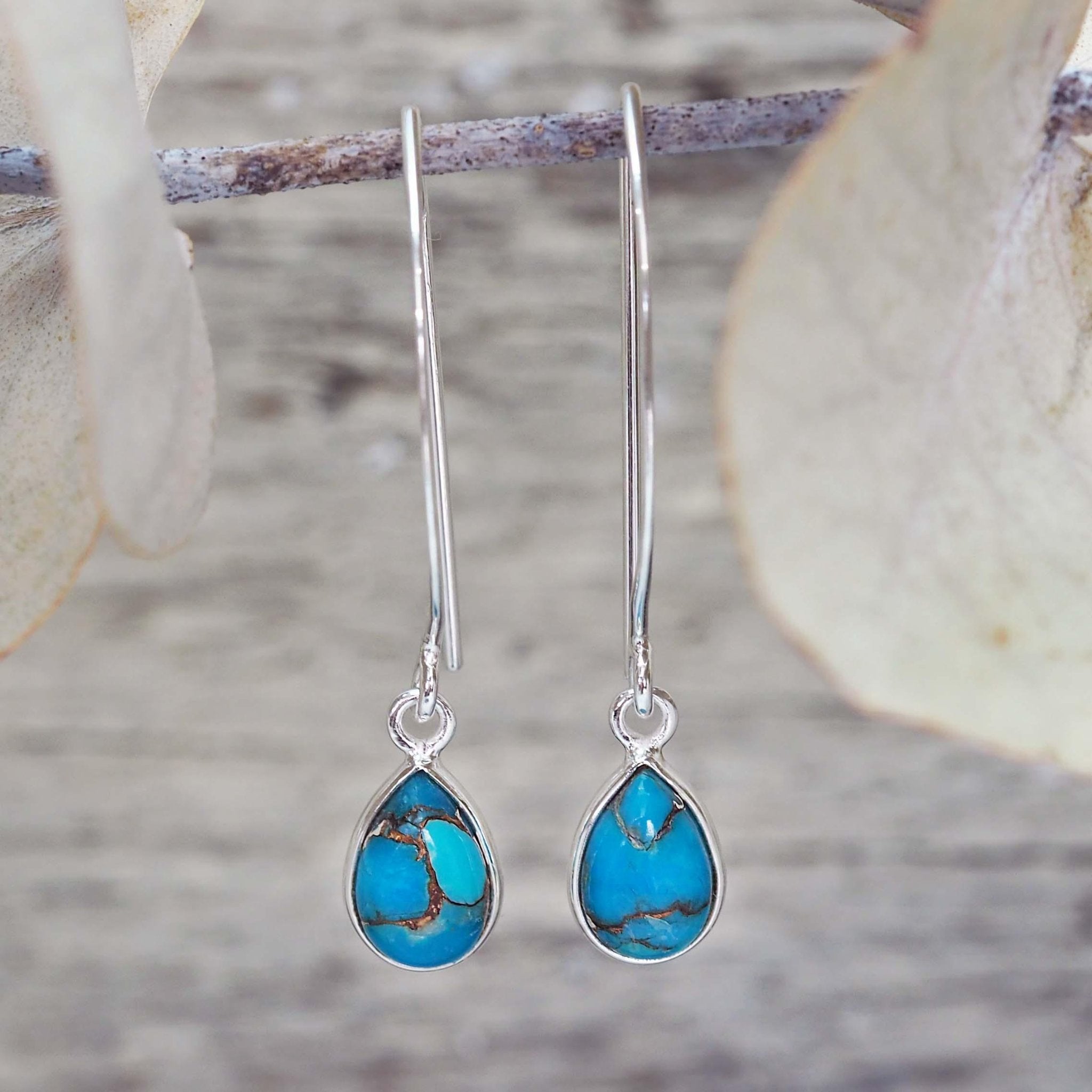 Turquoise teardrop earrings with silver hooks on a natural background