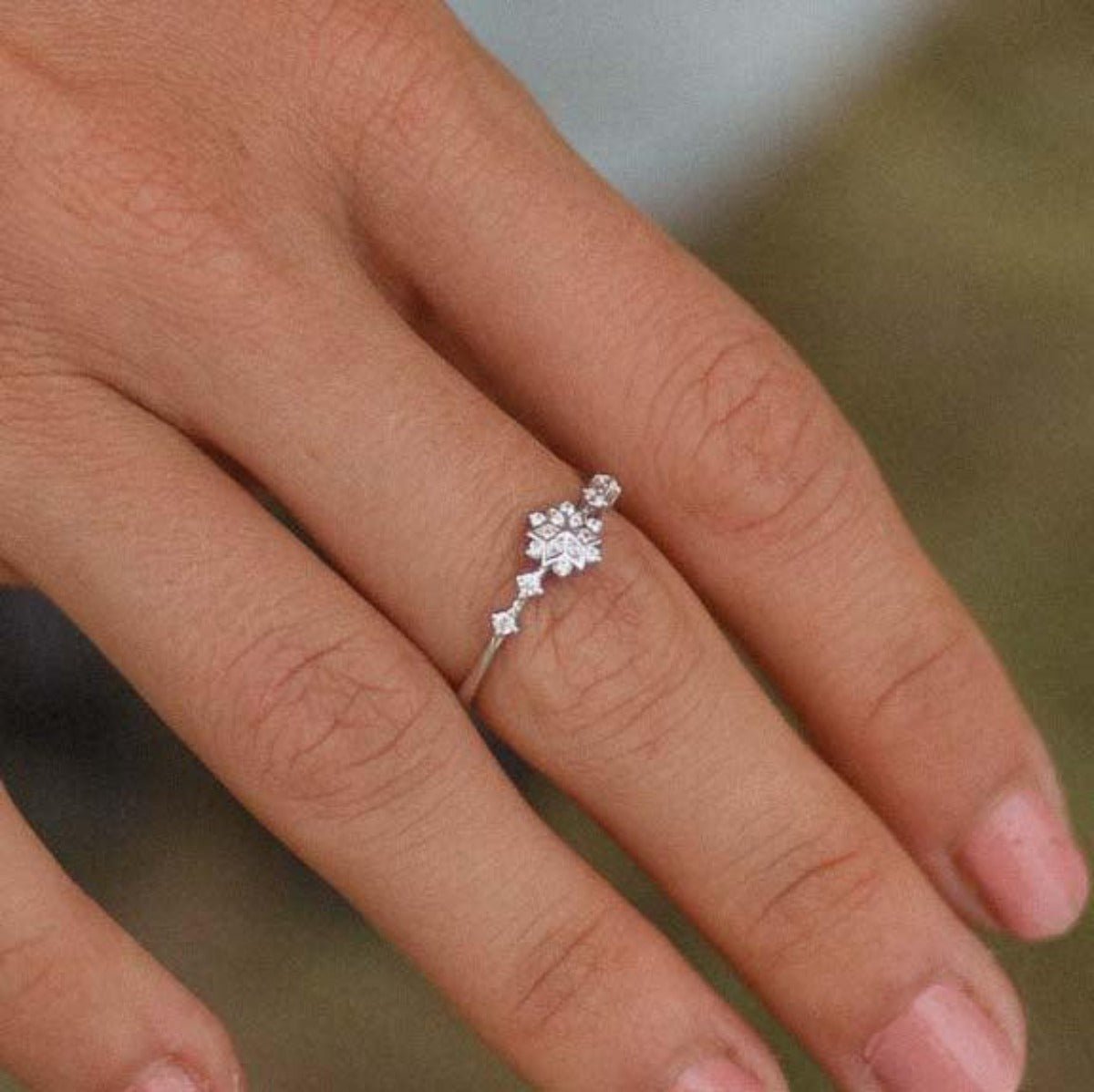 Finger wearing a dainty sterling silver ring with a delicate snowflake celestial cubic zirconia gemstone design
