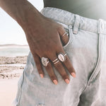 Hand wearing Cowrie Sea Shell Ring, sterling silver wave ring and moonstone ring with ocean in the background - indie and harper
